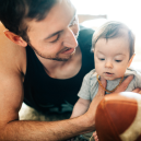 A father holds a football for his infant child.