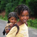A young Ethiopian girl smiles with her sibling on her back.