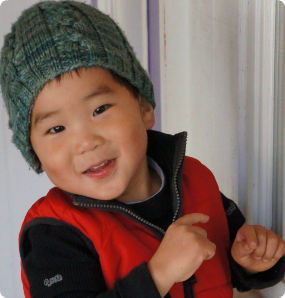 A little boy adopted from Korea in a wool cap and red vest.