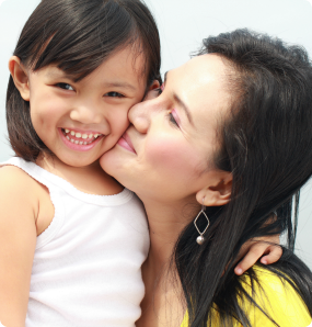 An Asian mother kisses her daughter on the cheek.