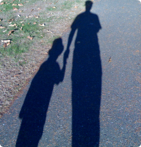 Shadows on a sidewalk of a child and parent holding hands.