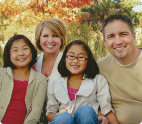 Jill, her husband, and two daughters who were adopted are pictured in front of fall leaves.