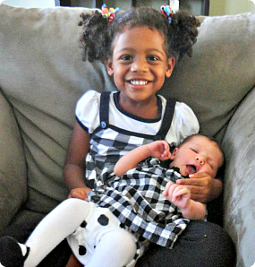 Faith smiles while holding her infant sister on the couch.