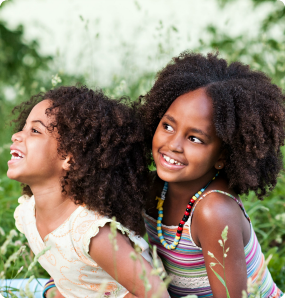 Tania and Meski, sisters adopted from Colombia and Ethiopia, smile big in a green field.