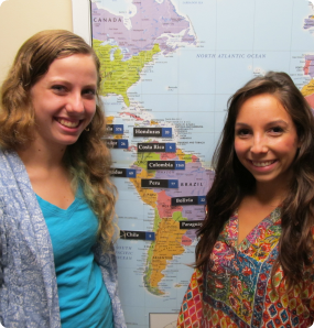 Two of our interns smile in front of a map that marks how many adoptions have taken place in each country.
