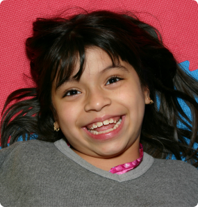 A nine-year-old girl from Latin America smiles on a mat.