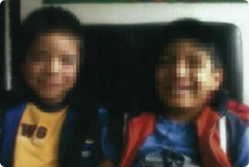 A blurred photo of Y and J, , who wait in Latin America for an adoptive family, sitting on a chair together.