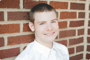 A picture of Jacob, a teen waiting for adoption from foster care, smiling in front of a brick wall.