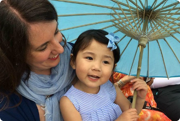 A picture of Gia, who was adopted from China and since undergone surgery to fix a heart defect, and her mother under a parasol.