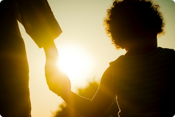 A silhouette of a white adoptive mother holding her black son's hand at sunset.