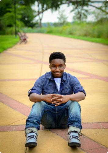 A picture of Michael, who waits in foster care for an adoptive family, sitting on the sidewalk.