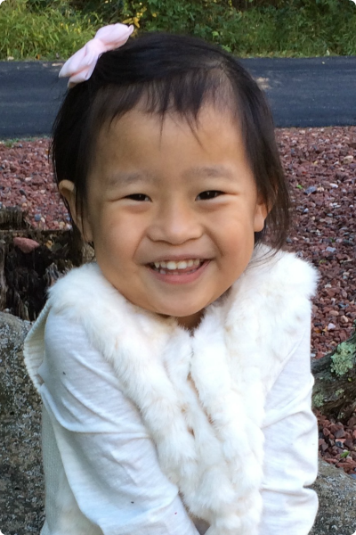A girl adopted from China smiles and shrugs her shoulders.