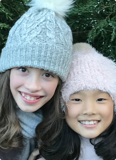 Two sisters, one adopted from South Korea, in winter hats.