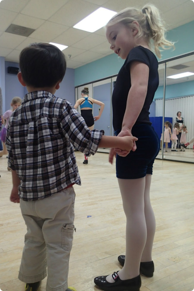 A sister holds her brother's hand at her dance class.