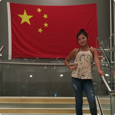 A teen adopted from China, smiling in front of a Chinese flag.