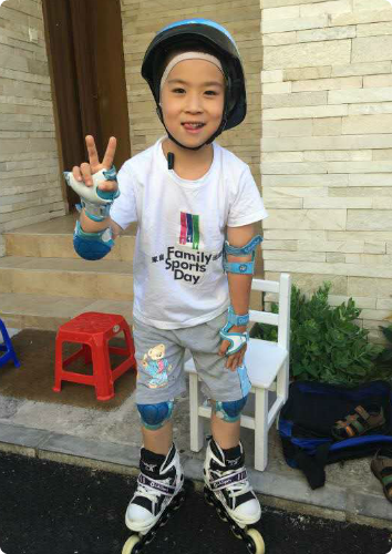 A picture of K, who waits to be adopted from Asia, wearing roller blades, a helmet, elbow pads and holding up a peace sign.