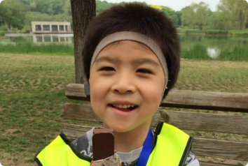 A picture of K, who waits in Asia for a family, smiling in a park with a chocolate ice cream sandwich.