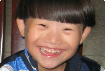 A photo of DW's face, smiling huge. He's wearing a jacket with different shades of blue and his hair is cut into a bowl cut. He's waiting in Asia for an adoptive family.