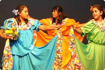 Three teenage girls dance in traditional Latin American clothing.