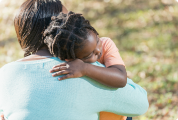 A young black boy hugs his foster mother's shoulder with his head turned to the right.