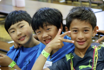 Three Korean adoptee boys who are about 10 years old, smile for the camera at Kamp Kimchee. One makes a peace sign as well.
