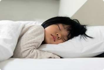 An Asian adoptte falls back asleep after a nightmare in her bed covered in white bedding.