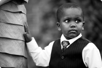 Lisa's son stands with his hand on his mother's dress and looking to the left. He is of African descent and dressed in a tie, vest and button up shirt. Photo credit Kara Pennington Photography.