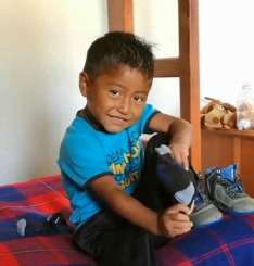 The youngest brother smiles at the camera as he puts on socks.