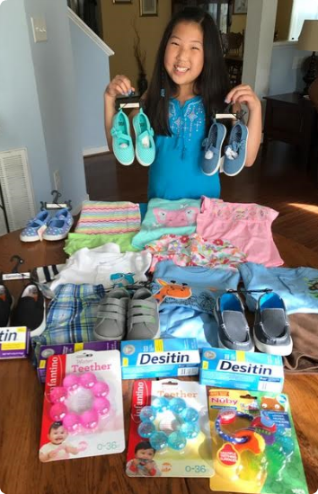 Kate, an 11-year-old Korean adoptee, stands in front of a pile of baby clothes, diaper cream and other items she bought with her birthday money to donate to Korean foster care.