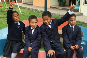 Four siblings who wait for parents in Latin America are pictured wearing suits and sitting in a park.