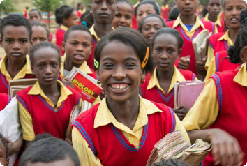 A young teen girl grins widely at the camera while in a crowd of her classmates. They all wear new uniforms provided by Adams Thermal Foundation.