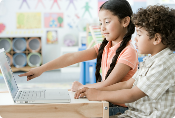 Two school aged children of Latinx descent sit in front of a computer.
