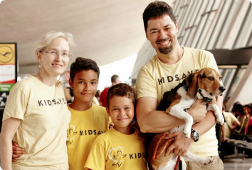 A Kidsave host family is pictured with children waiting for adoption who are visiting from Colombia. The host dad is holding a dog in his arms and everyone is wearing Kidsave shirts.