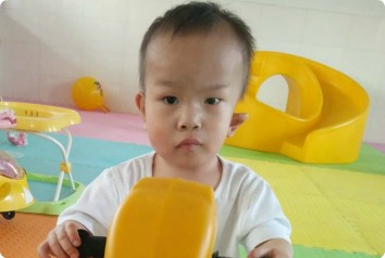SW, a 3-year-old boy waiting to be adopted, is pictured sitting on yellow rocking horse.