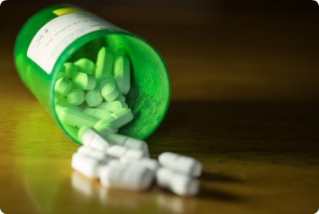 A close-up image of an open green bottle of opioid prescription medication. The pills are spilling out of it onto the table.