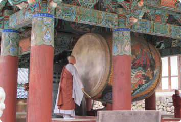 A picture of a monk next to a giant drum in South Korea.
