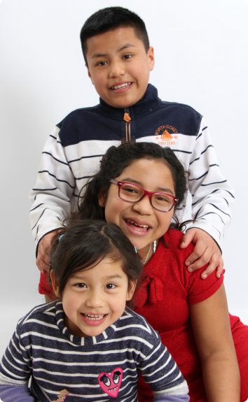 Three siblings, adopted together internationally, line up to be photographed with big smiles.