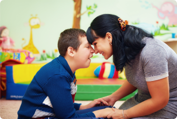 A woman providing emergency shelter care, leans her forehead against the forehead of a boy with developmental disabilities that is in her care.