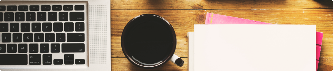 A laptop keyboard is pictured next to a cup of black coffee and a notebook as someone prepares to watch a webinar.