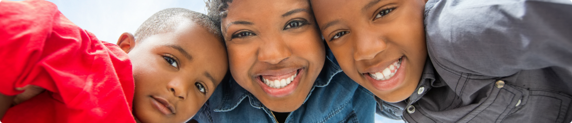 An African American mother smiles with her arms around her two adopted sons from foster care.