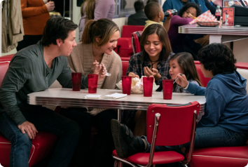 A still frame from the film, Instant Family, with the family sitting at a diner. Here's what you can do after the movie.