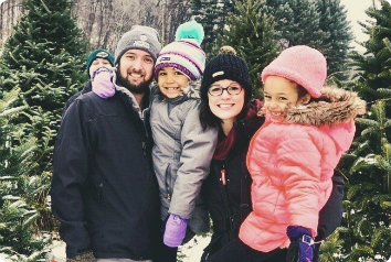 Ashley, Frank and their daughters adopted from foster care smile among pine trees in the snow.