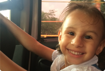 S smiles big while riding a bus. She waits for an adoptive family.