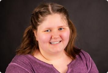 Sherakey smiles with pigtails in her hair against a grey background.