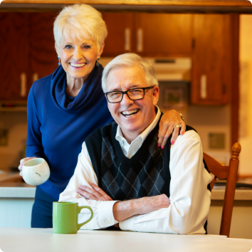 Karen and John smile in their kitchen. They've been fostering infants for 34 years.