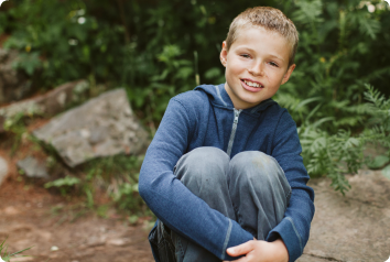 Mathew, who waits in foster care, smiles while sitting in the woods.