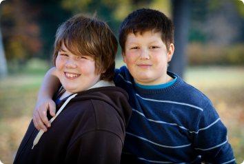 Two boys in Minnesota foster care smile in the park. One has his arm around the other's shoulder.
