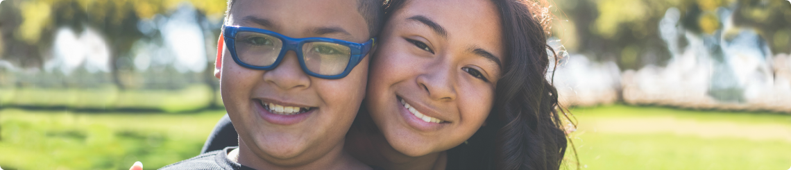 A brother and sister in foster care waiting to be adopted are smiling in the park.