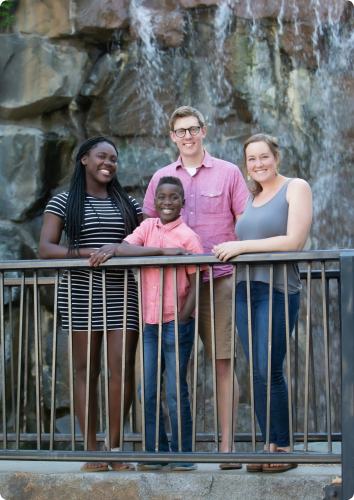 A young couple smile with their children in front of a waterfall. The children were adopted from MN foster care.