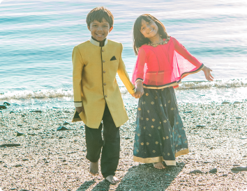 A brother and sister adopted together from India smile on the beach.